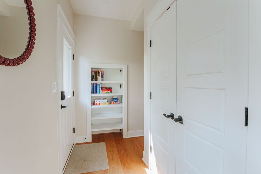 A hallway with a white door, a bookshelf with books and boxes, and a wooden floor.