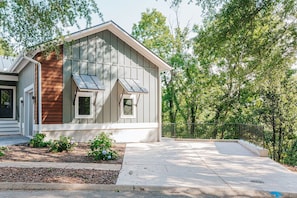 Una casa de una sola planta con un porche delantero, un pequeño jardín con flores y una cerca de metal al fondo.