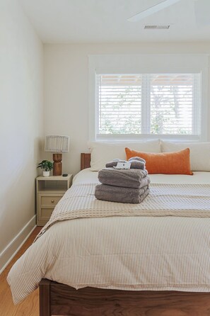 Un dormitorio con una cama, una mesita de noche, una lámpara y una ventana con persianas.