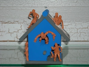 Ein Spielzeughaus mit Figuren auf dem Dach und einer Figur davor.
