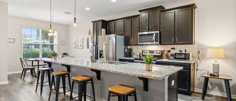 Una cocina moderna con una isla central, taburetes de bar, microondas y refrigerador.