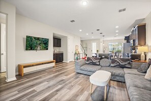 Ein großzügiges Wohnzimmer mit einer breiten Eckcouch, einem weißen Couchtisch und einem flachbildfernseher, der an der Wand befestigt ist.
