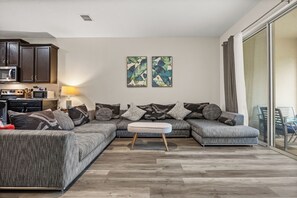 Ein modernes Wohnzimmer mit einer Eckcouch, einem kleinen Tisch und einer Küchenzeile inklusive Geräte.