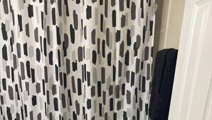 Ein Badezimmer mit Toilette, einer Duschvorhang mit einem schwarz-weißen abstrakten Muster und einer schwarzen Badmatte auf dem Boden.