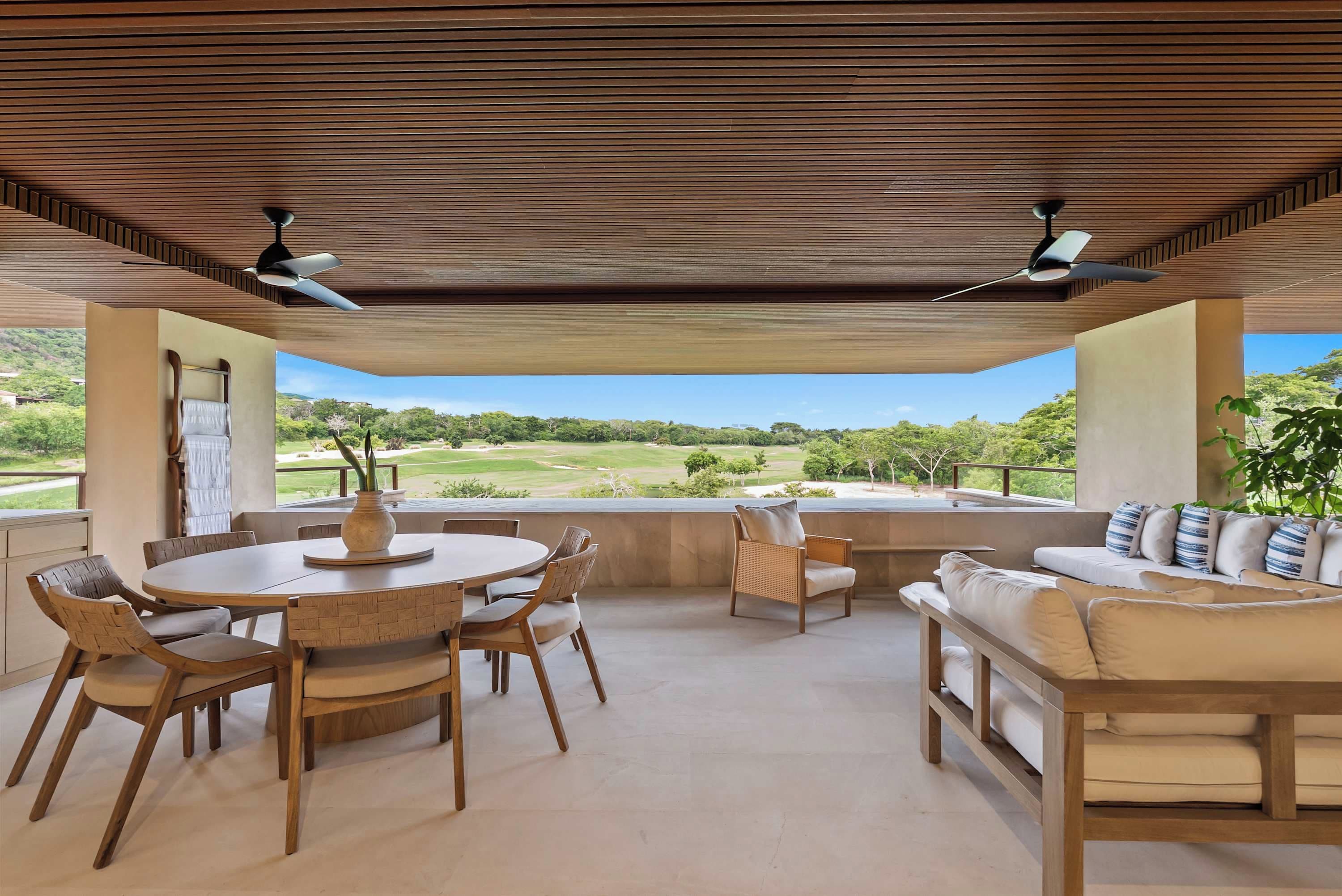 Um pátio externo com mesa redonda e cadeiras, um sofá, e vista para um campo de golfe.