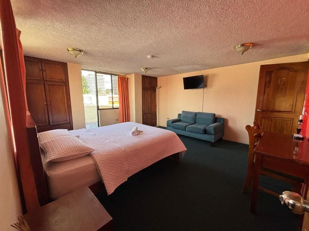 Una habitación de hotel con cama, sofá, televisor y un armario de madera.
