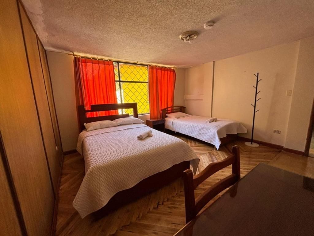 Une chambre avec deux lits, un plancher en bois, une fenêtre avec des rideaux rouges et une lampe.