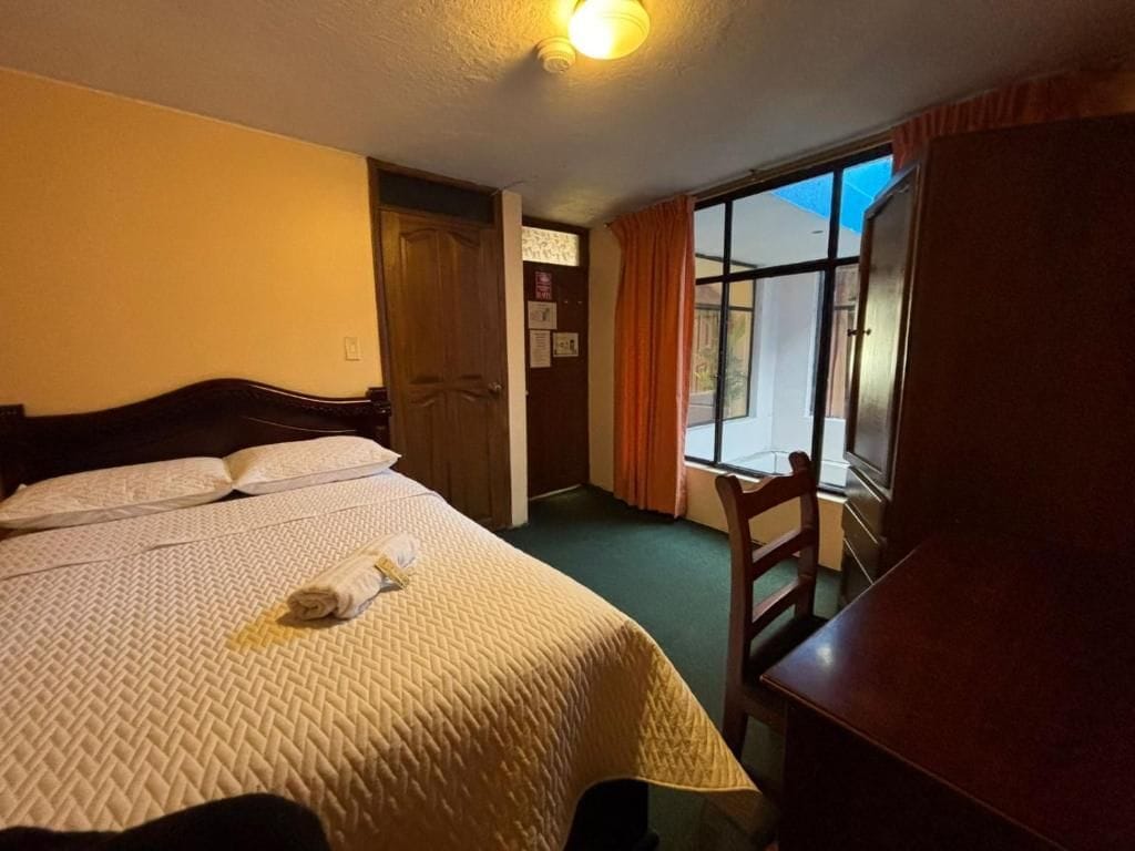 A hotel room with a bed, a desk, a chair, and a window.