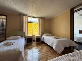 Quarto de hotel com duas camas de solteiro, janela com cortinas, piso de madeira e vista para o exterior.