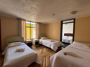 Habitación de hotel con tres camas individuales, piso de madera tipo espiga, ventana con cortinas y vistas al exterior.