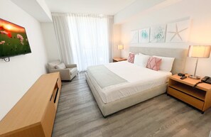 A hotel room with a bed, a desk, a chair, a TV, and artwork on the wall. - Cozy 1BR Resort Amenities, Beach Access & Pool (Hallandale Beach)