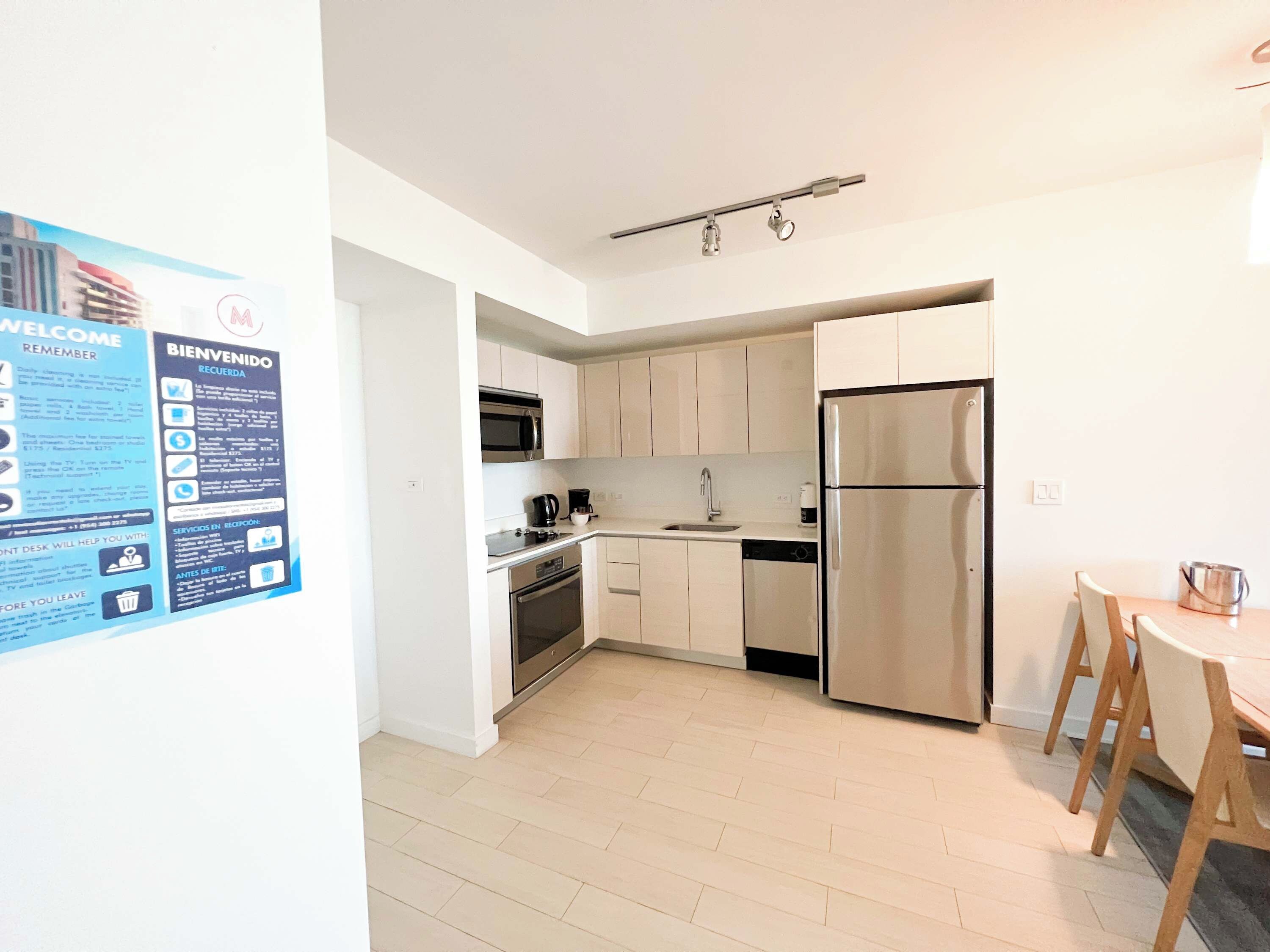 A modern kitchen with stainless steel appliances, a dishwasher, and a dining area with a wooden table and chairs.