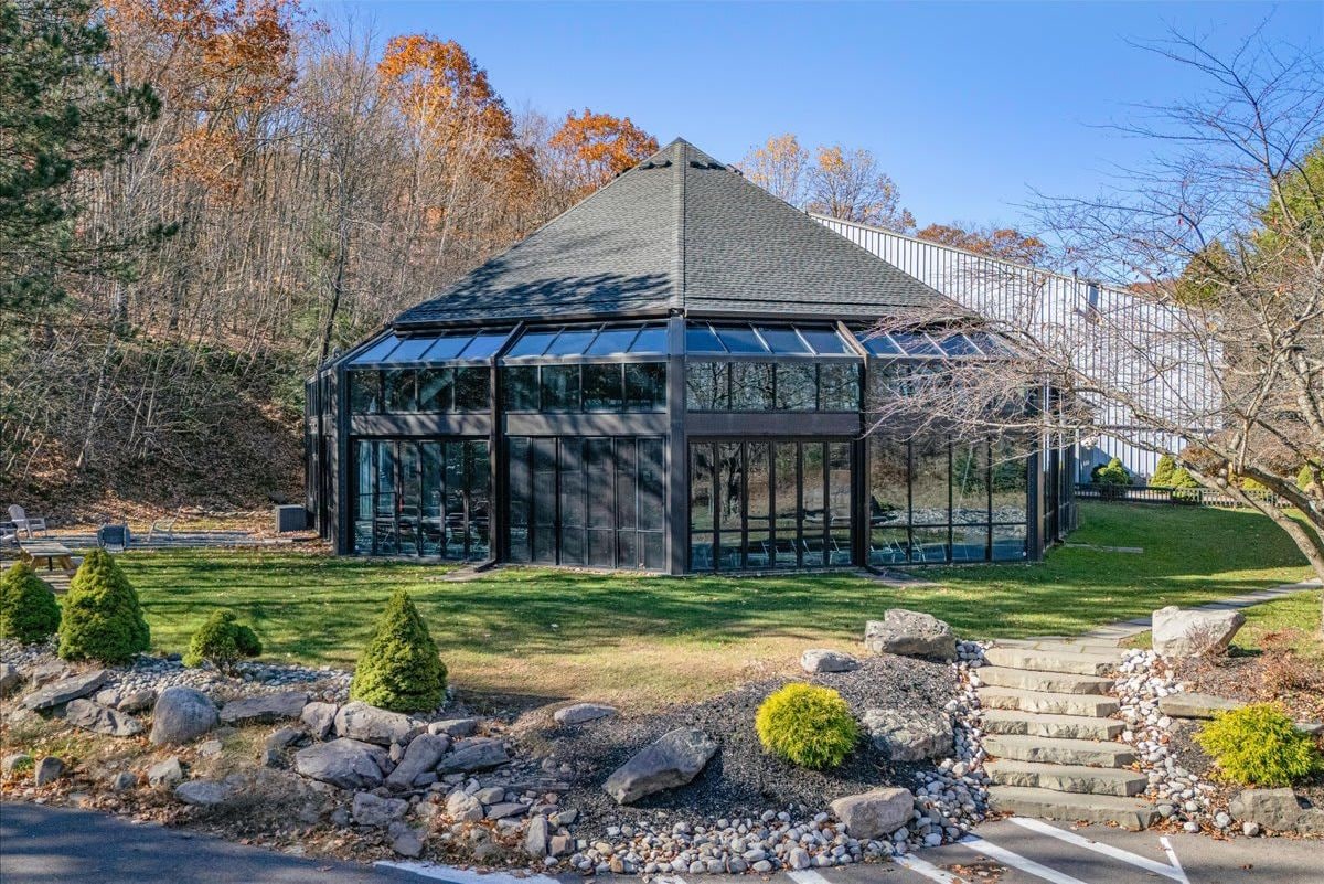 A modern glass conservatory with a stone roof, surrounded by a landscaped garden with rocks and shrubs.