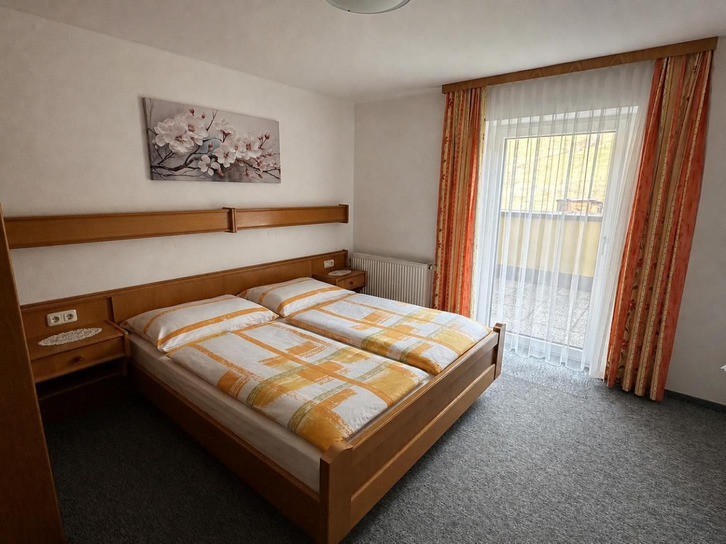 Ein Doppelbett mit Holz Kopfteil, ein Nachttisch, ein Heizkörper und ein Fenster mit Vorhängen.
