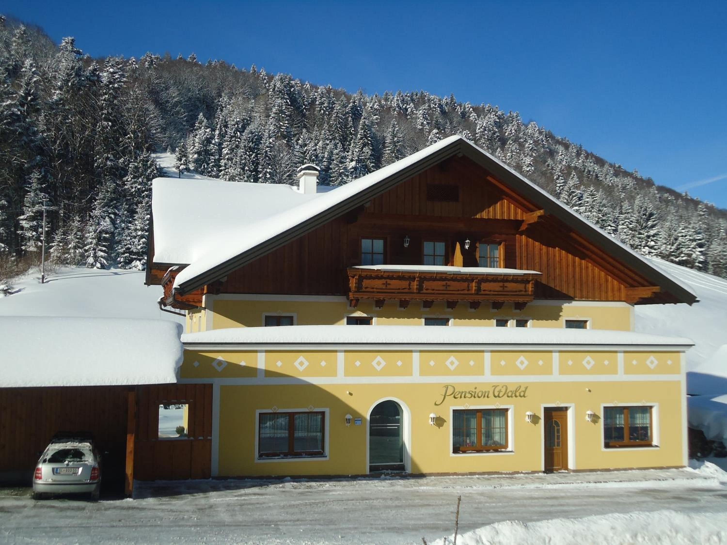 Ein zweistöckiges Gebäude mit einer gelben Fassade und einem hölzernen Balkon, mit der Aufschrift 'Pension Wald'.