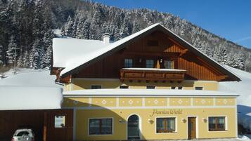 Ein zweistöckiges Gebäude mit einer gelben Fassade und einem hölzernen Balkon, mit der Aufschrift 'Pension Wald'.