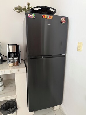 Ein schwarzer Kühlschrank mit Magneten, einer Kaffeemaschine und einem Mülleimer.