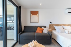 A modern living room with a grey sofa, a wooden coffee table, and a bed with white bedding. - Studio Mabouya, Vue mer (Sainte-Luce)