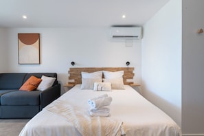 A modern hotel room with a bed, a sofa, a wall-mounted air conditioner, and a painting. - Studio Mabouya, Vue mer (Sainte-Luce)