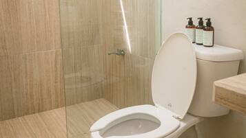 Un baño moderno con cabina de ducha de vidrio, inodoro y artículos de aseo en la encimera.