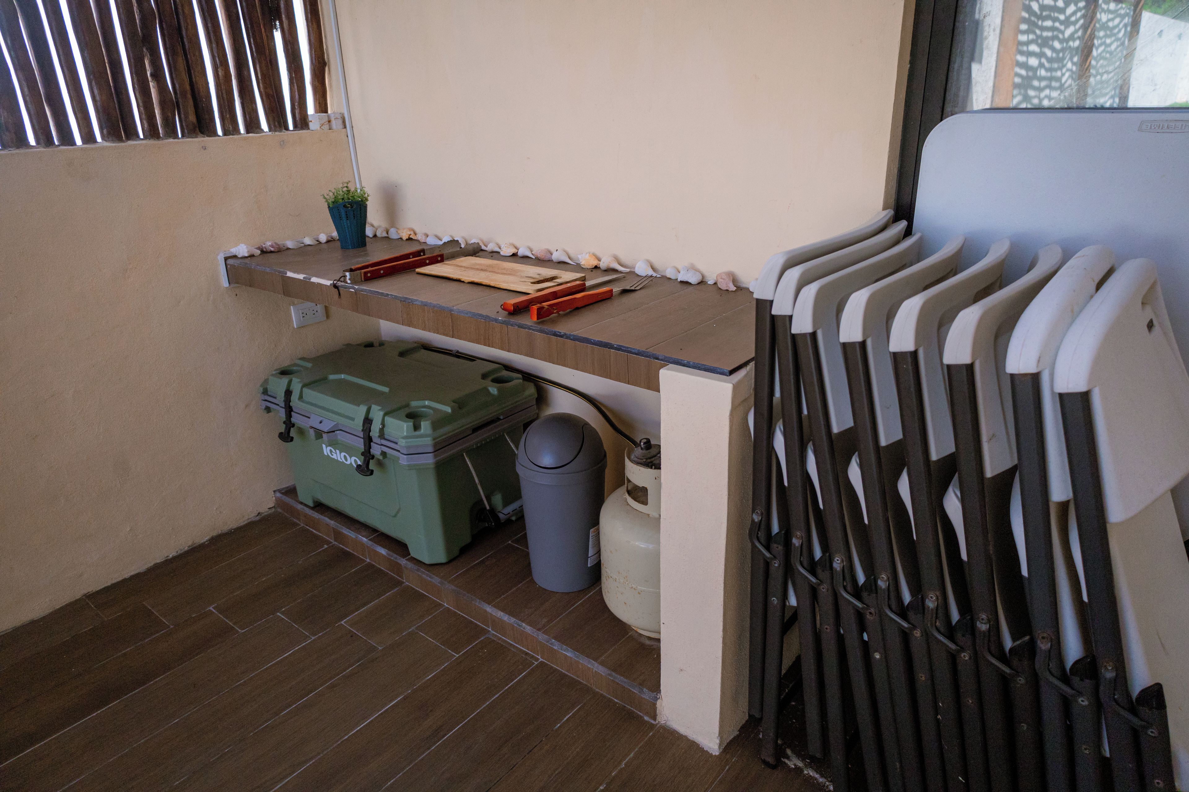A small kitchenette with a countertop, a green storage box, a trash bin, and a window with barred glass.
