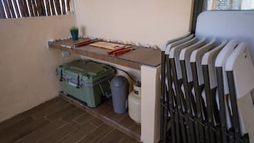 A small kitchenette with a countertop, a green storage box, a trash bin, and a window with barred glass.