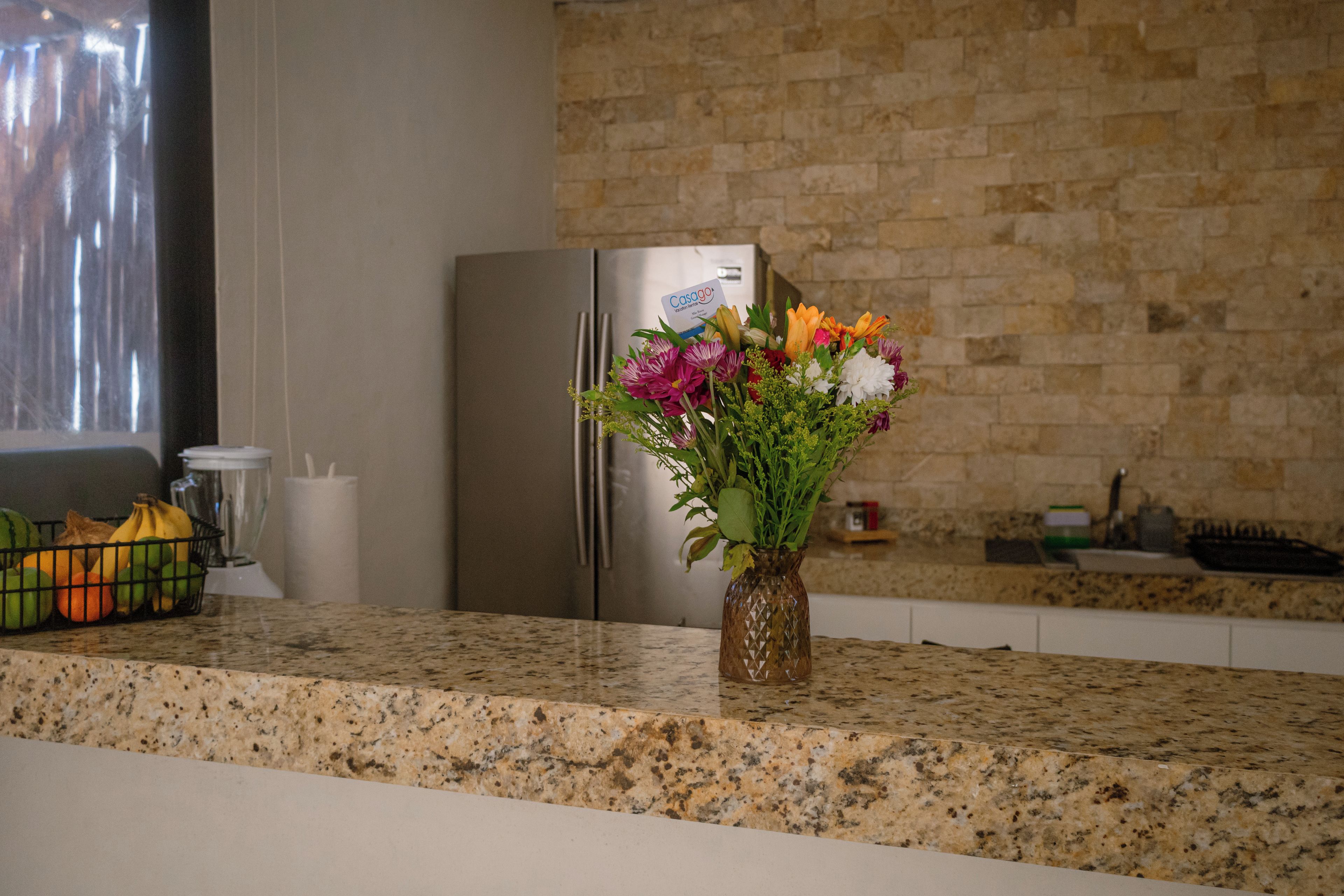 A kitchen with a granite countertop, a stainless steel refrigerator, and a vase with flowers.