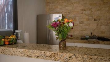 A kitchen with a granite countertop, a stainless steel refrigerator, and a vase with flowers.