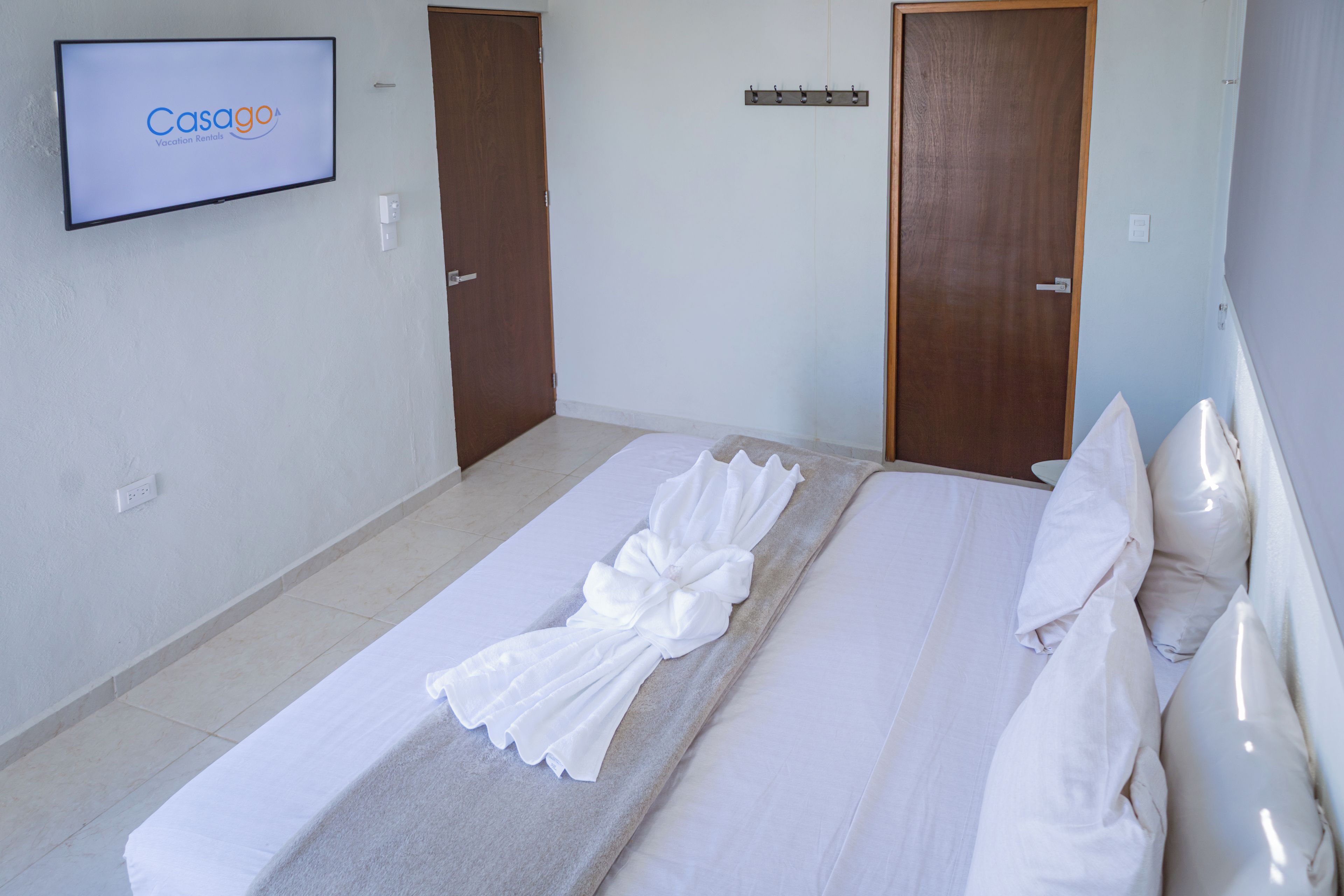 A hotel room with a bed, a TV displaying 'CasaGo Vacation Rentals', and two doors.