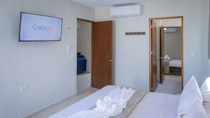 Quarto de hotel com cama, televisão na parede e porta para o banheiro.