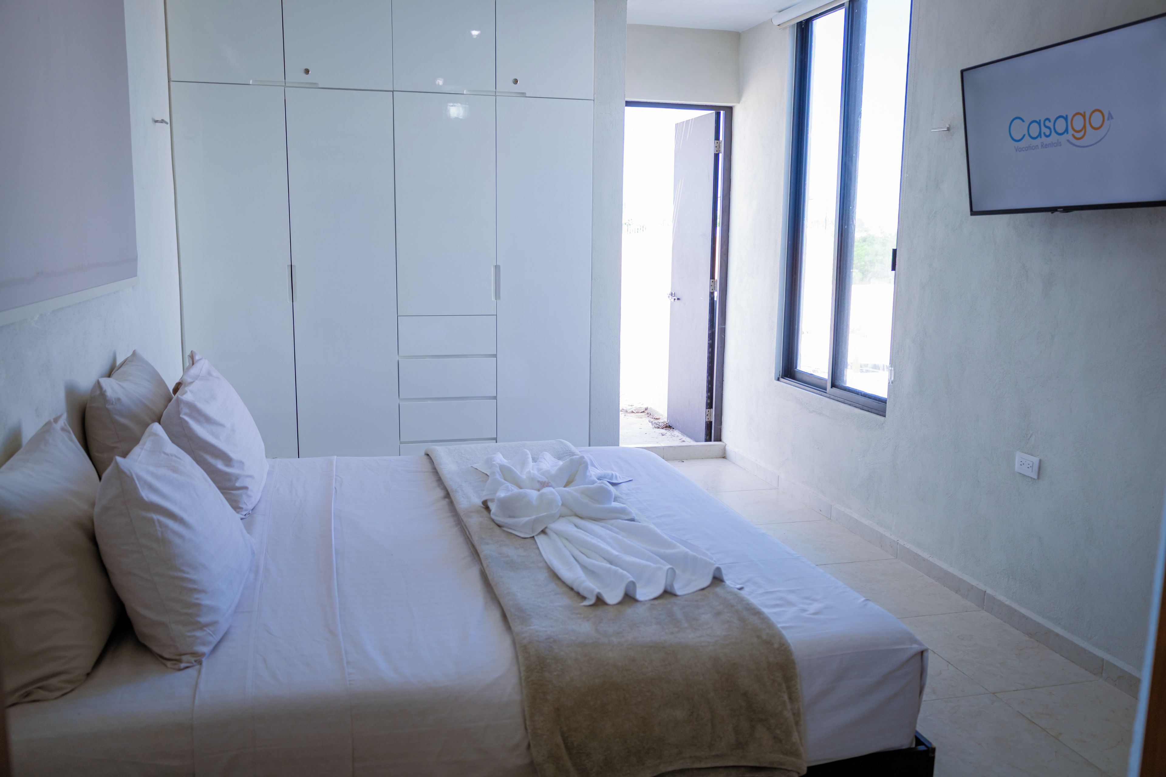 Ein Hotelzimmer mit Bett, Kissen, Bademantel, Kleiderschrank und einem Fernseher, der den Markennamen zeigt.