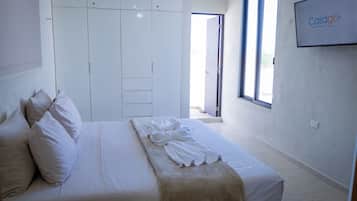 Ein Hotelzimmer mit Bett, Kissen, Bademantel, Kleiderschrank und einem Fernseher, der den Markennamen zeigt.