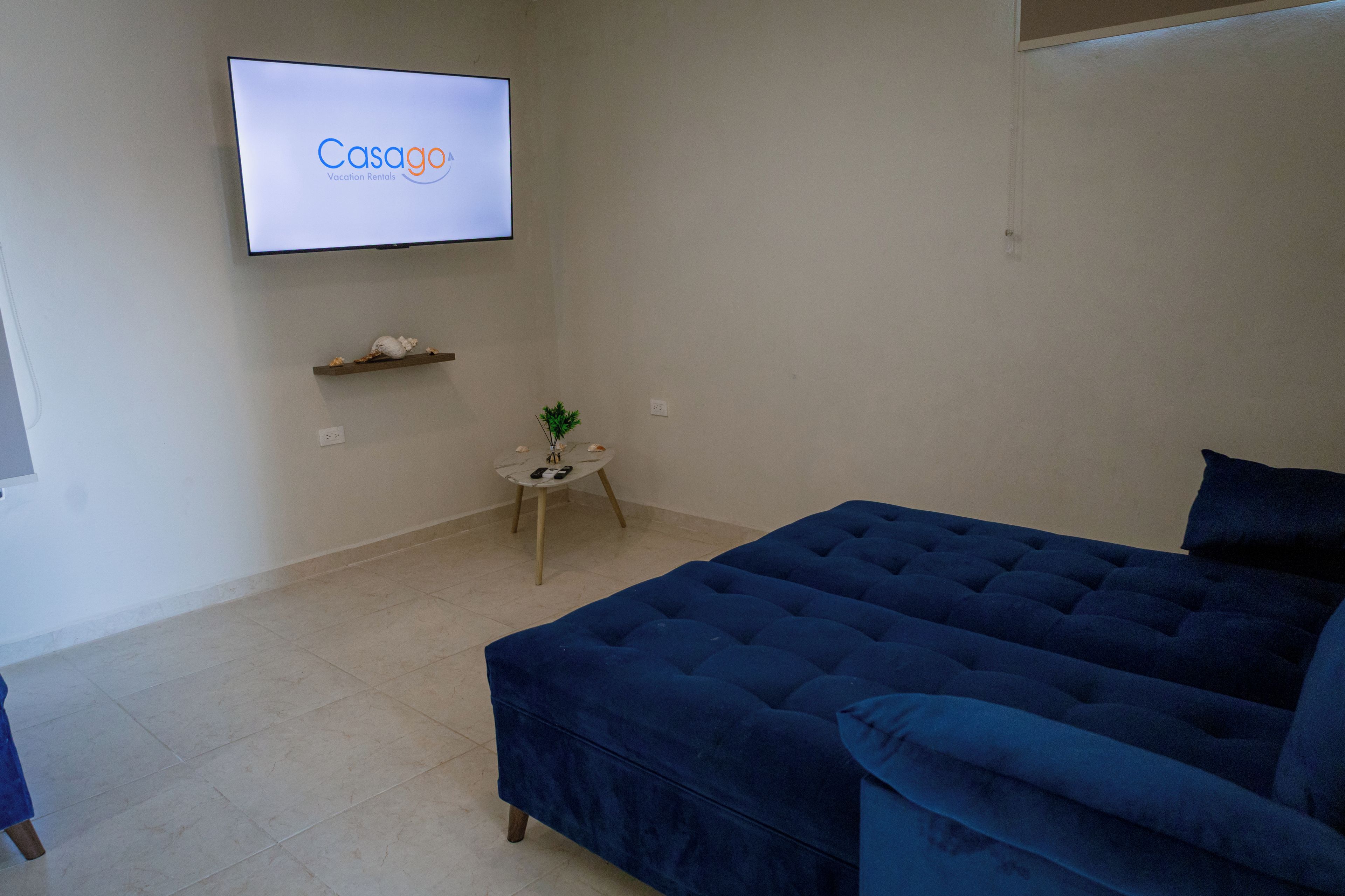 A room with a large bed, a small table with a plant, and a TV displaying 'Casago Vacation Rentals'.