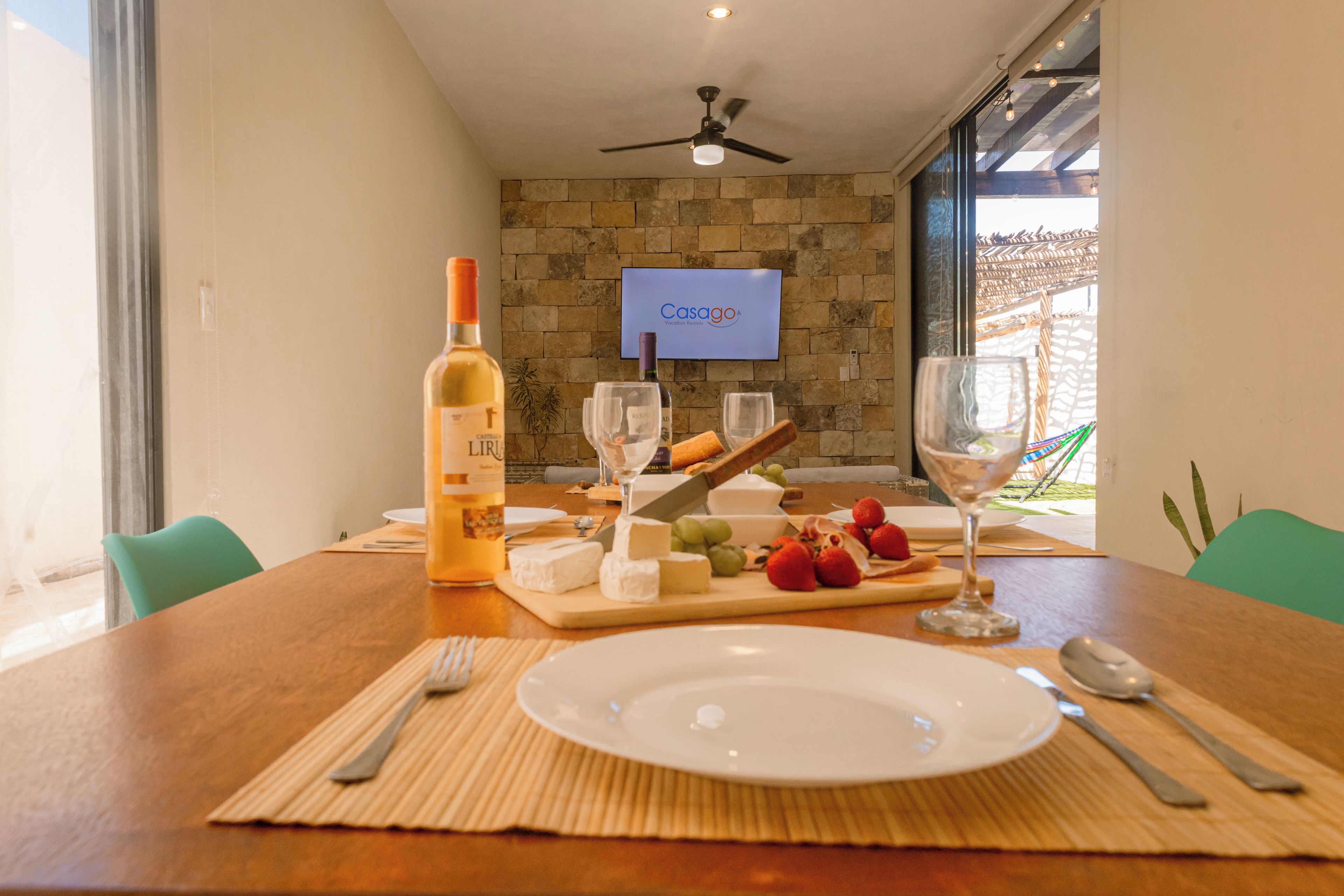 A dining table with a bottle of wine, cheese, grapes, and strawberries, set for a meal.