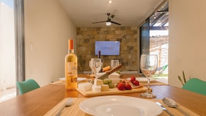 Mesa de jantar posta para uma refeição, com garrafa de vinho, queijo, uvas e morangos.