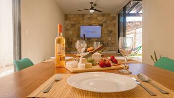 A dining table with a bottle of wine, cheese, grapes, and strawberries, set for a meal.