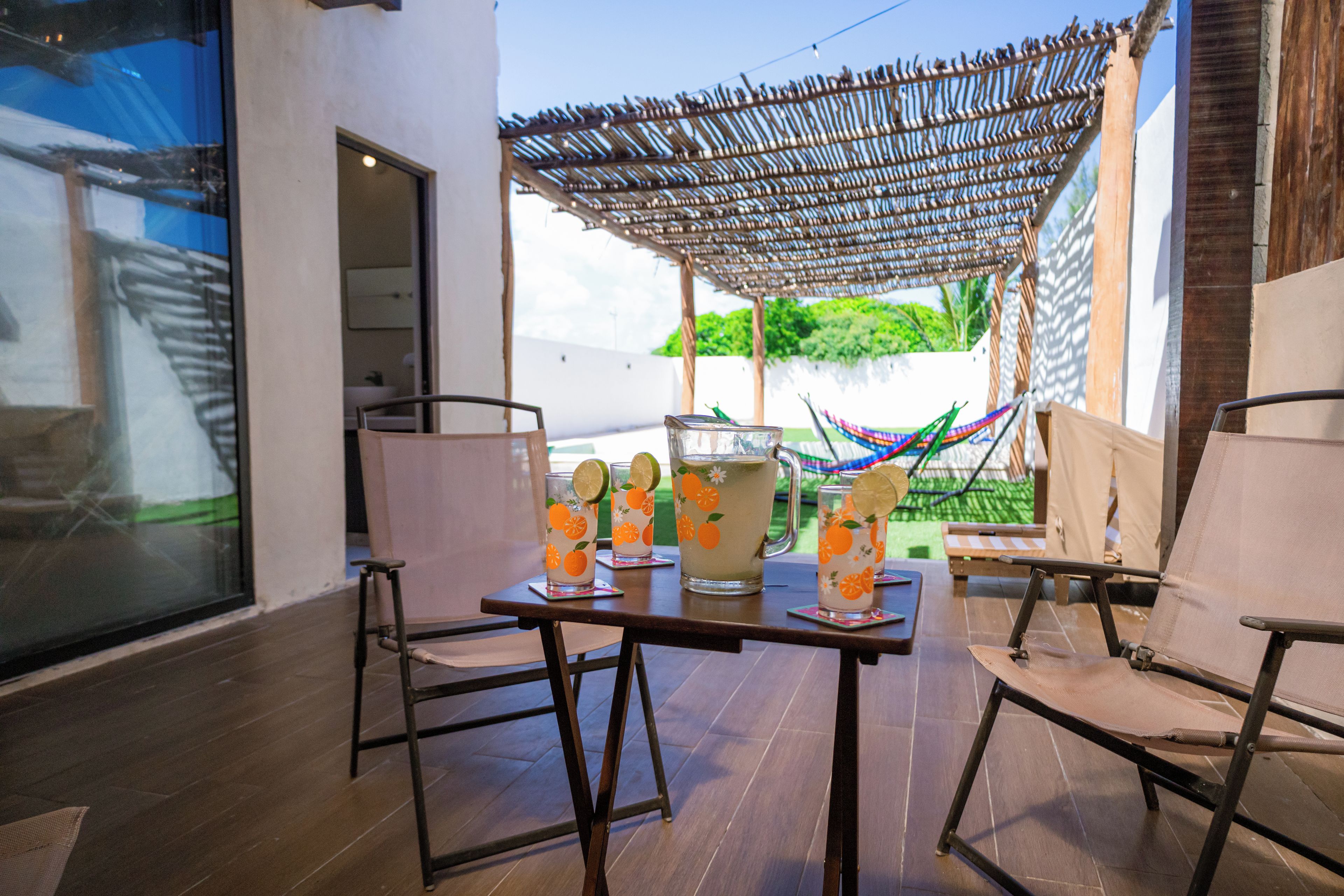 Un espacio al aire libre con una mesa para dos, con un parasol tejido y dos vasos de una bebida adornada con lima.