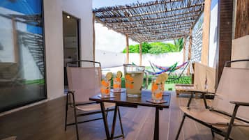 A patio area with a table set for two, featuring a woven umbrella and two glasses of a beverage with a lime garnish.