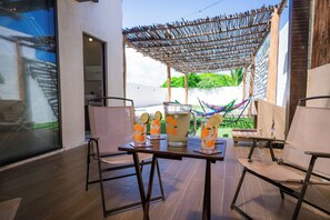 Un espacio al aire libre con una mesa para dos, con un parasol tejido y dos vasos de una bebida adornada con lima.