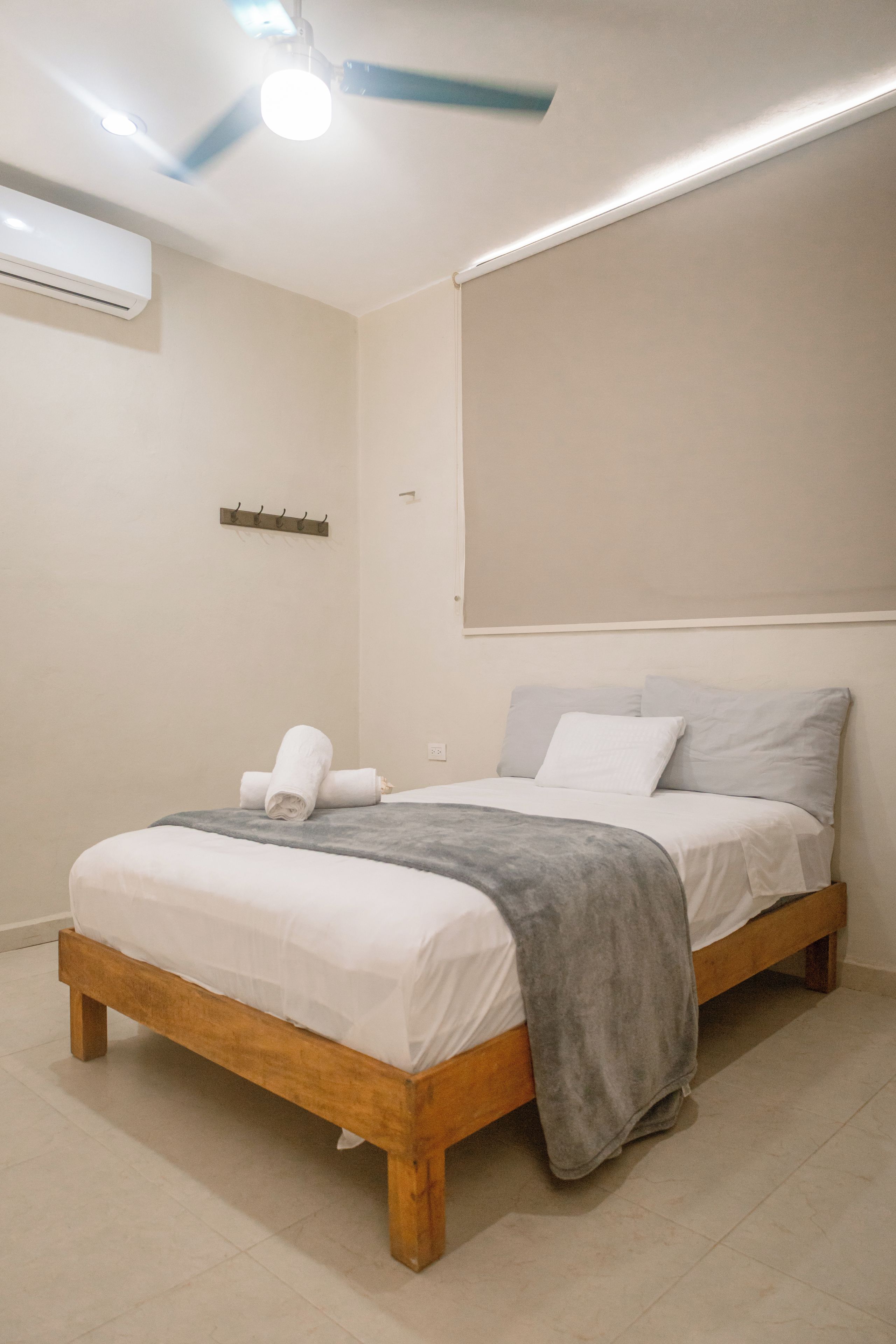 A bedroom with a wooden bed, a grey blanket, and a ceiling fan.