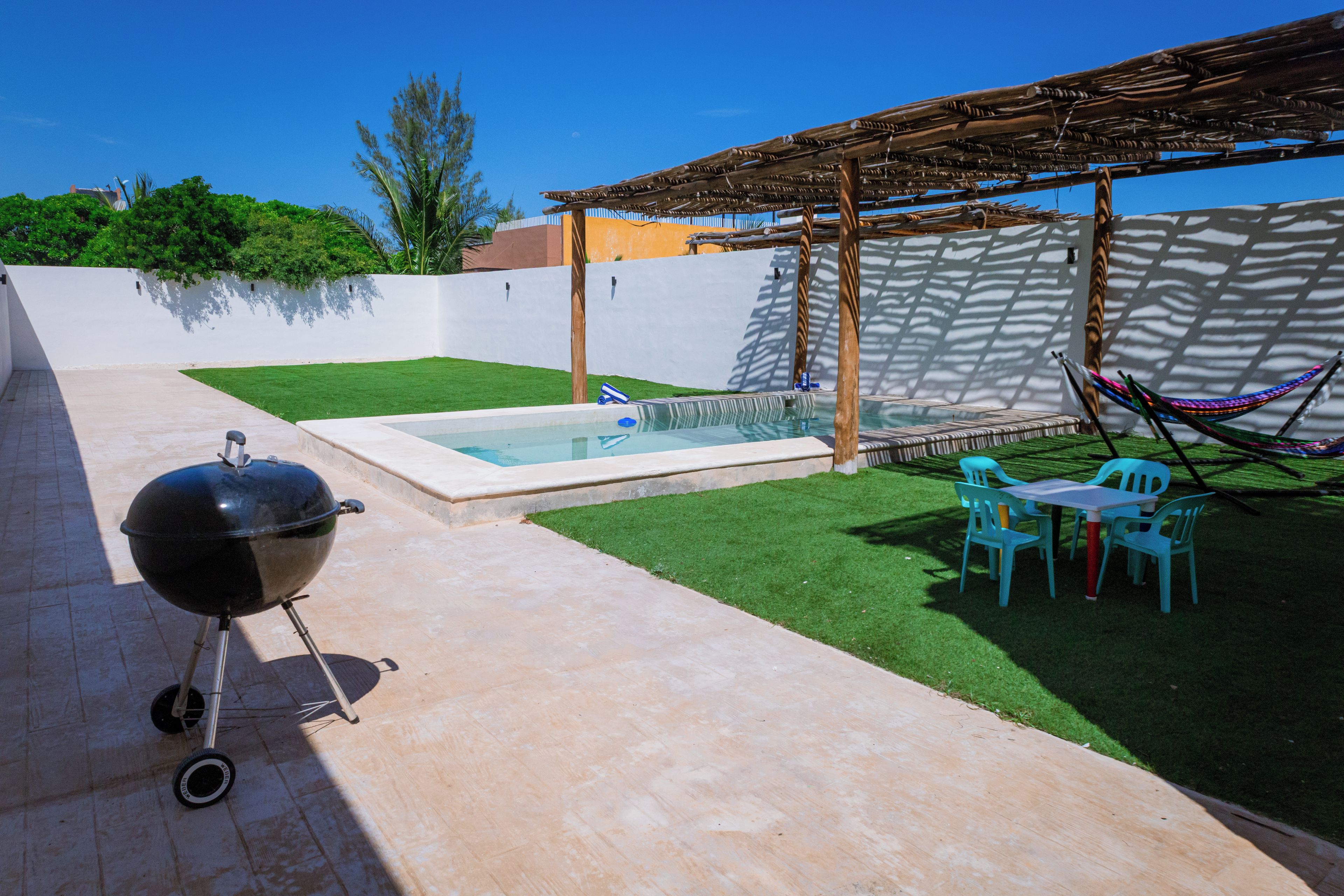 Une terrasse avec un barbecue, une petite piscine et un hamac.