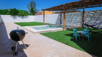 Une terrasse avec un barbecue, une petite piscine et un hamac.