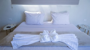 Cama bem arrumada com roupa branca e toalha dobrada em laço sobre a cama.