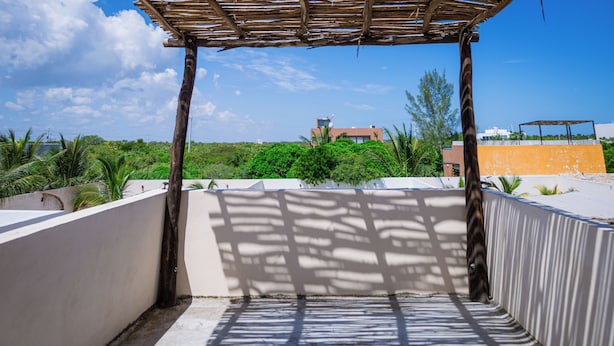 Terraço no telhado com pérgola, vista para áreas verdes e edifícios ao fundo.