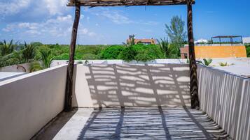 A rooftop terrace with a pergola structure, a view of greenery and buildings in the background.