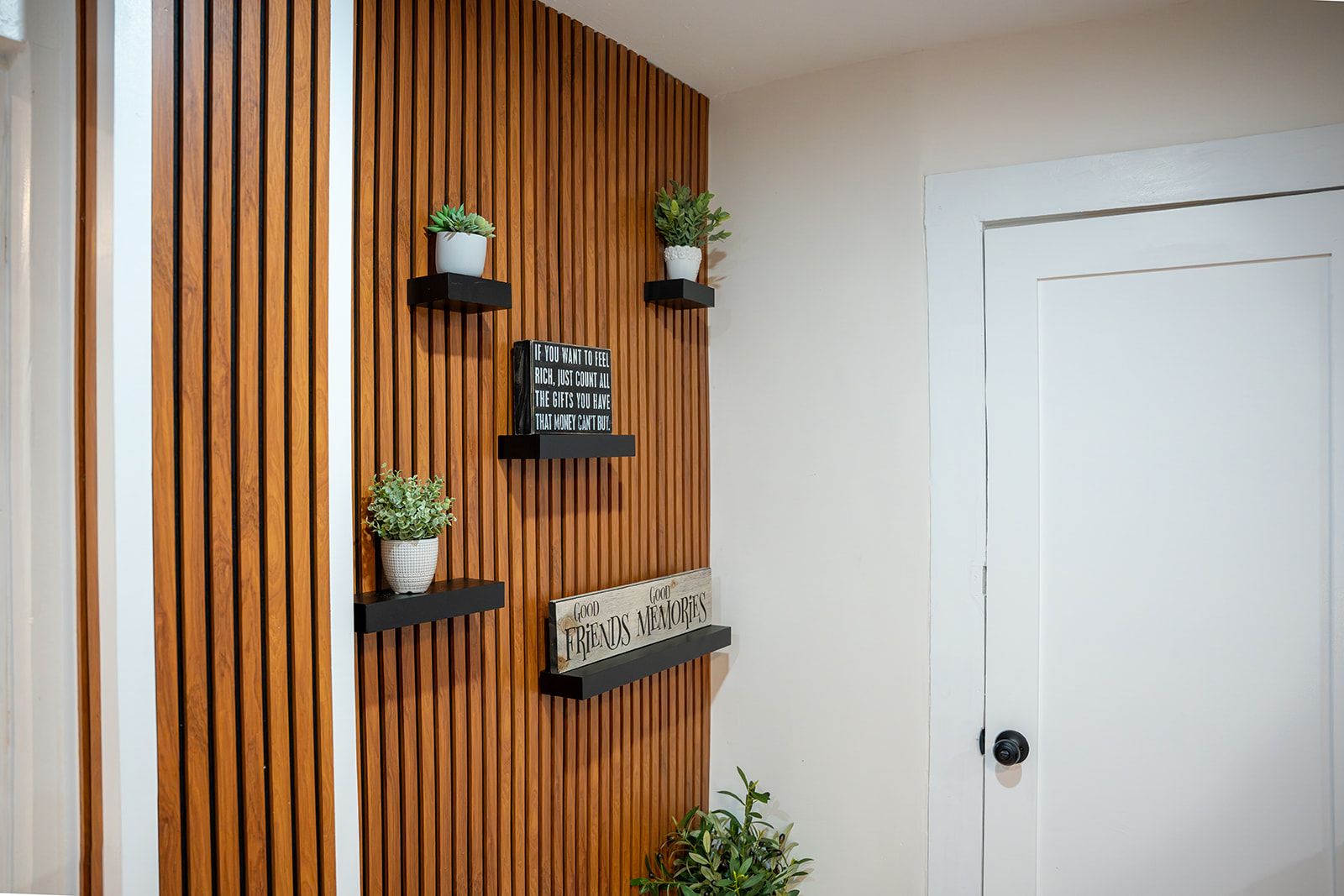A wall with vertical wooden slats, three black shelves with potted plants, and two signs with motivational quotes.