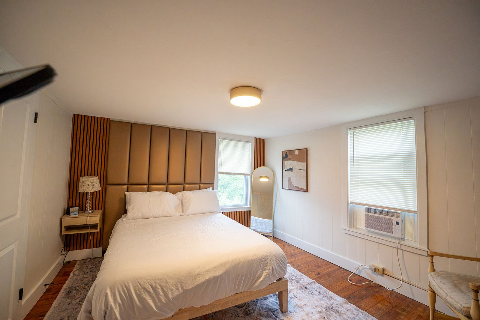 A bedroom with a bed, bedside table, lamp, mirror, window, and radiator.