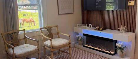 Un salon avec une cheminée, deux fauteuils en bois, une table basse et un téléviseur à écran plat fixé au mur.