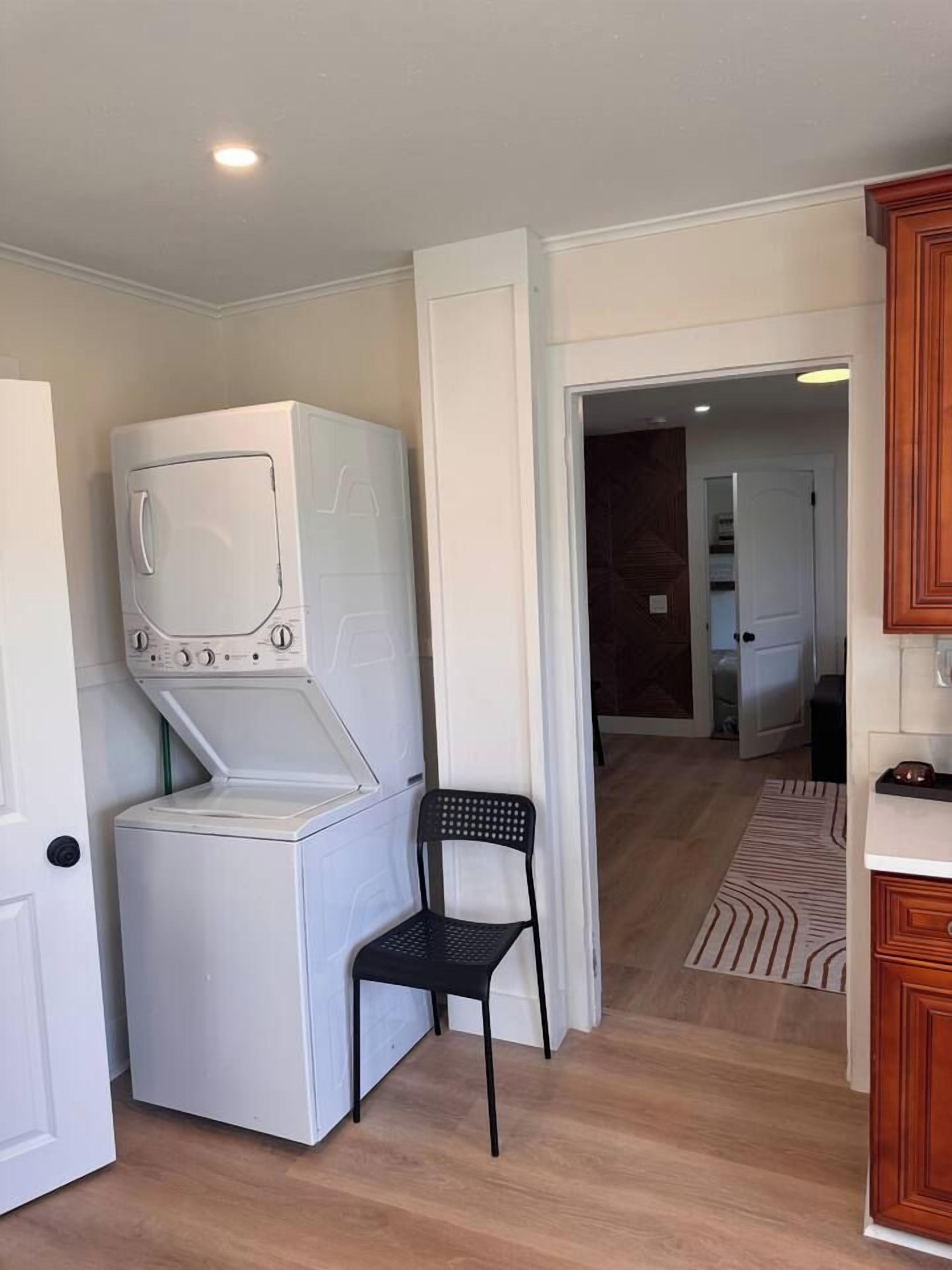 A laundry room with stacked washer and dryer, a black chair, and a wooden cabinet.
