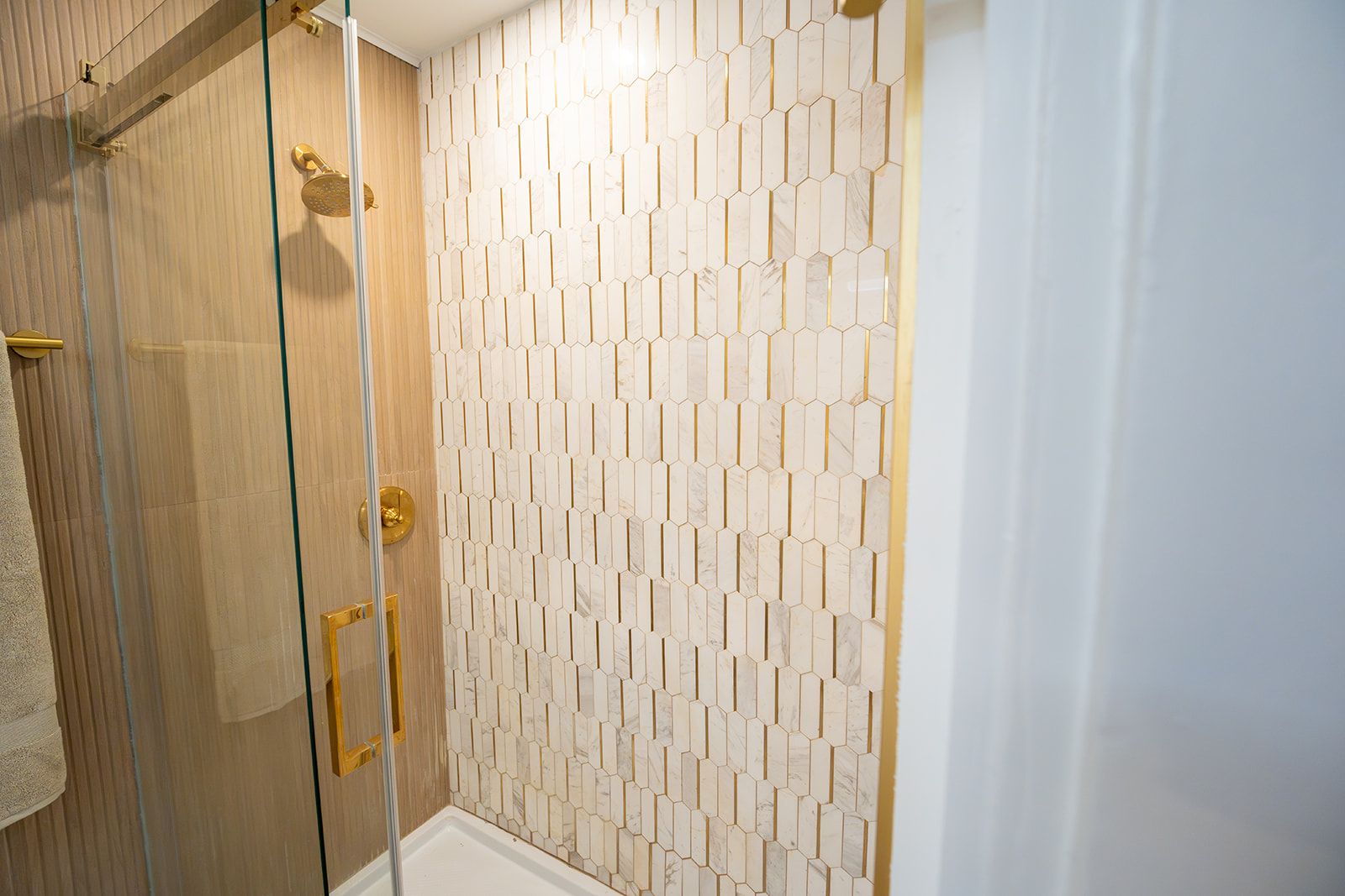 A shower area with a glass door, a wooden door, and a tiled wall with a geometric pattern.